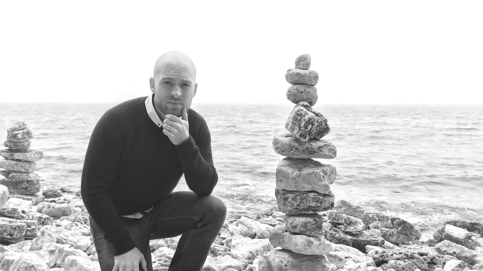 Daniel Morell looking pensive on a beach with a cairn.